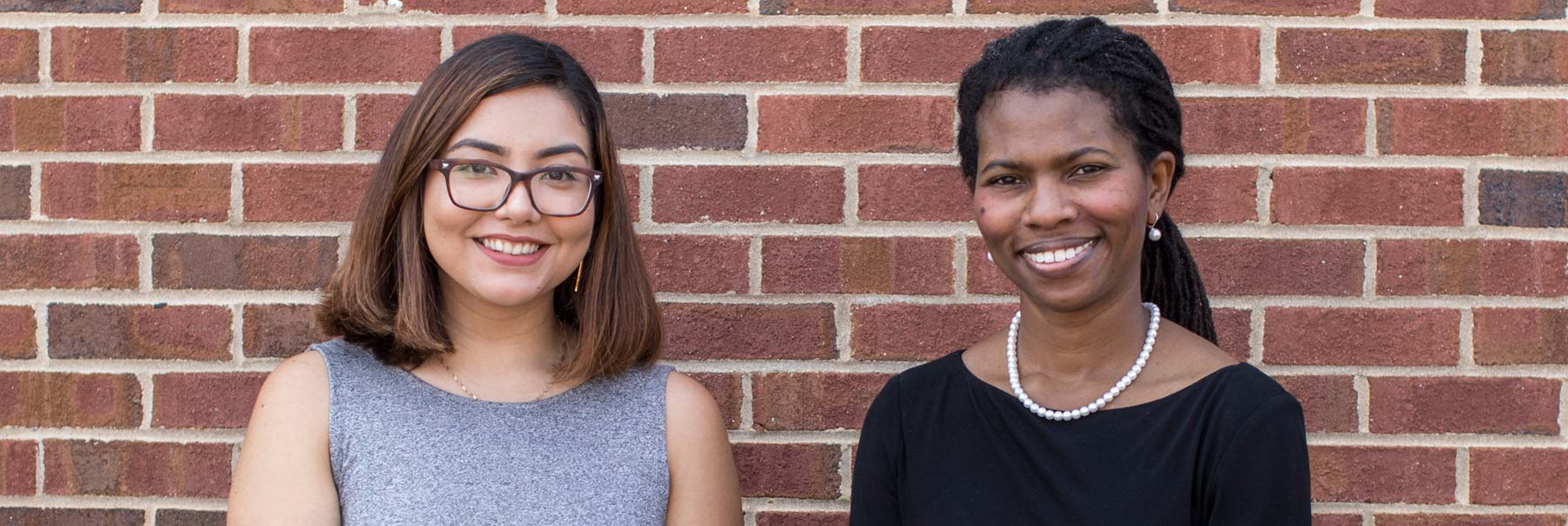 Lilian posing with another woman outside against a red brick wall